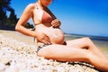 Pregnant woman skin care moisturizer cream on belly on beach at Royalty Free Stock Photo