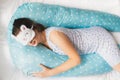 Pregnant woman sleeps in nightgown in bed on blue comfortable supporting pillow with stars. Funny sleeping white mask in form of