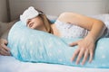 Pregnant woman sleeps in nightgown in bed on blue comfortable supporting pillow with stars. Funny sleeping white mask in form of