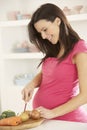 Pregnant Woman Slicing Vegetables In Kitchen At Home