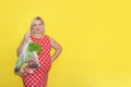 pregnant woman with a smile holds a shopping bag with vegetables and fruits in her hand on a yellow background with copy Royalty Free Stock Photo