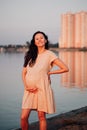 Pregnant woman smiles. Happy young beautiful Asian woman with long dark hair stands on beach, touches her stomach and Royalty Free Stock Photo