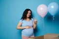 Pregnant woman smiles strokes belly shows two fingers at camera, feeling positive emotions expecting twins. Gender party Royalty Free Stock Photo