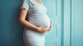 Pregnant woman smiling and holding her big belly caringly against blue wall background. Generative AI Royalty Free Stock Photo