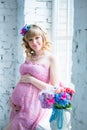 Pregnant woman smiling, looking at belly, holding flowers. Pink dress. Royalty Free Stock Photo