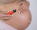 A pregnant woman smokes a vape. A girl holds an electronic cigarette against the background of her bare tummy.