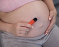 A pregnant woman smokes a vape while sitting on the couch. Close-up of the abdomen.