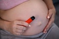 A pregnant woman smokes a vape while sitting on the couch. Close-up of the abdomen.