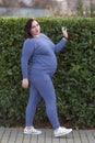 Pregnant woman in sportswear walks along clipped shrubbery