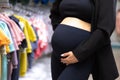 Pregnant woman standing at clothing store. Mother doing shopping in baby shop and looking at camera. Baby clothes sale and Royalty Free Stock Photo