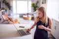 Pregnant Woman Standing By Kitchen Counter Working From Home On Laptop Royalty Free Stock Photo