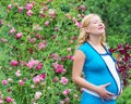 Pregnant woman standing near a bush with roses