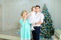 Pregnant woman standing near husband keeping little daughter near Christmas tree.