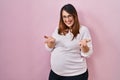 Pregnant woman standing over pink background smiling cheerful offering hands giving assistance and acceptance