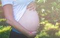 Pregnant woman standing and touching her belly in the park. Close-up of torso. Future mom expecting baby. Maternity