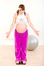 Pregnant woman standing on weight scale at home