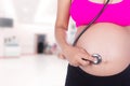 pregnant woman with stethoscope listening belly to baby in hospital background Royalty Free Stock Photo