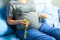 Pregnant woman with a stomach and holding donut and yellow measuring tape. Diet for pregnant women.