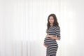 Pregnant woman in striped dress holds hands on belly on a white background. Pregnancy, maternity, preparation and expectation conc