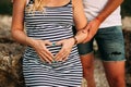 Pregnant woman in a striped dress makes her hands on her belly heart