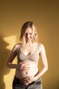 Pregnant woman stroking her tummy - over yellow background Royalty Free Stock Photo