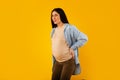 Pregnant woman suffering from pain, having spasm during painful contractions, touching back over yellow background Royalty Free Stock Photo