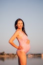 pregnant woman in a swimsuit, portrait of a young beautiful pregnant woman in a pink swimsuit on the beach in summer at Royalty Free Stock Photo