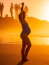 Pregnant woman in swimwear posing on beach with bright sunrise or sunset and trees on background Royalty Free Stock Photo