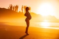 Pregnant woman in swimwear posing on beach with bright sunrise or sunset and trees on background Royalty Free Stock Photo