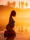 Pregnant woman in swimwear posing on ocean beach with bright sunrise or sunset Royalty Free Stock Photo