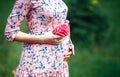 Pregnant woman touching bump whilst holding pink rose girl waiting