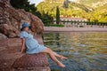 Pregnant woman traveler in denim dress, blue straw hat sits by the sea, dangles legs in water