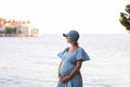 Pregnant woman traveler hugs baby in her belly near the island of Sveti Stefan in Montenegro