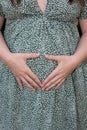 Pregnant woman tummy body in flower dress view hands make heart finger in belly pregnancy Royalty Free Stock Photo