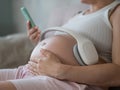 A pregnant woman turns on music for her child on a smartphone. Headphones on the tummy.