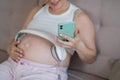 A pregnant woman turns on music for her child on a smartphone. Headphones on the tummy.