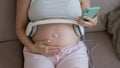 A pregnant woman turns on music for her child on a smartphone. Headphones on the tummy.