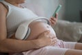 A pregnant woman turns on music for her child on a smartphone. Headphones on the tummy.