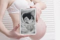 Pregnant woman in underwear holding and showing digital tablet with fetal ultrasound photo on white wooden background. Close-up