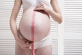 Pregnant woman in underwear measures belly using a measuring tape Royalty Free Stock Photo