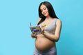 Pregnant woman in underwear writing in notebook against blue wall Royalty Free Stock Photo