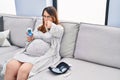 Pregnant woman using blood pressure monitor at home pointing with finger to the camera and to you, confident gesture looking