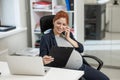 Pregnant woman using mobile phone and holding paper tablet in office. Royalty Free Stock Photo