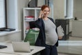 Pregnant woman using mobile phone and holding paper tablet in office. Royalty Free Stock Photo