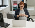 Pregnant woman using mobile phone in office. Royalty Free Stock Photo