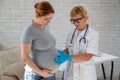 Pregnant woman visiting a doctor. Elderly Caucasian female gynecologist holds hands on the tummy of a pregnant patient. Royalty Free Stock Photo