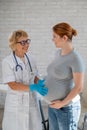 Pregnant woman visiting a doctor. Elderly Caucasian female gynecologist holds hands on the tummy of a pregnant patient Royalty Free Stock Photo