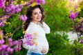 Pregnant woman walking in the autumn park. With one hand she hugs belly and touches flowers with other, she is looking Royalty Free Stock Photo