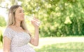 A pregnant woman is watching drinking water while sitting on a park bench. Royalty Free Stock Photo