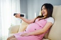 Pregnant woman watching tv with remote control on sofa in living room Royalty Free Stock Photo